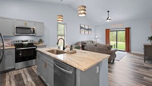 Una cocina moderna con electrodomésticos de acero inoxidable, encimera de mármol y comedor con sofá y ventilador de techo.