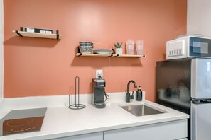 Une cuisine avec un plan de travail blanc, un évier, une machine à café, un four à micro-ondes et un réfrigérateur.