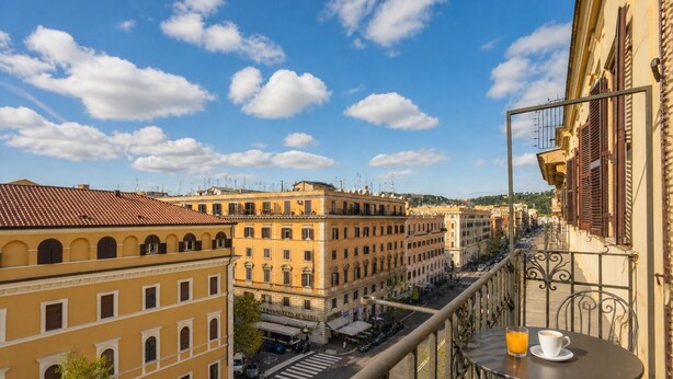 A balcony with a table, a cityscape view, and a building with a sign. - Michelangelo Prestige Apartment Vatican View by RHR (ROMA)