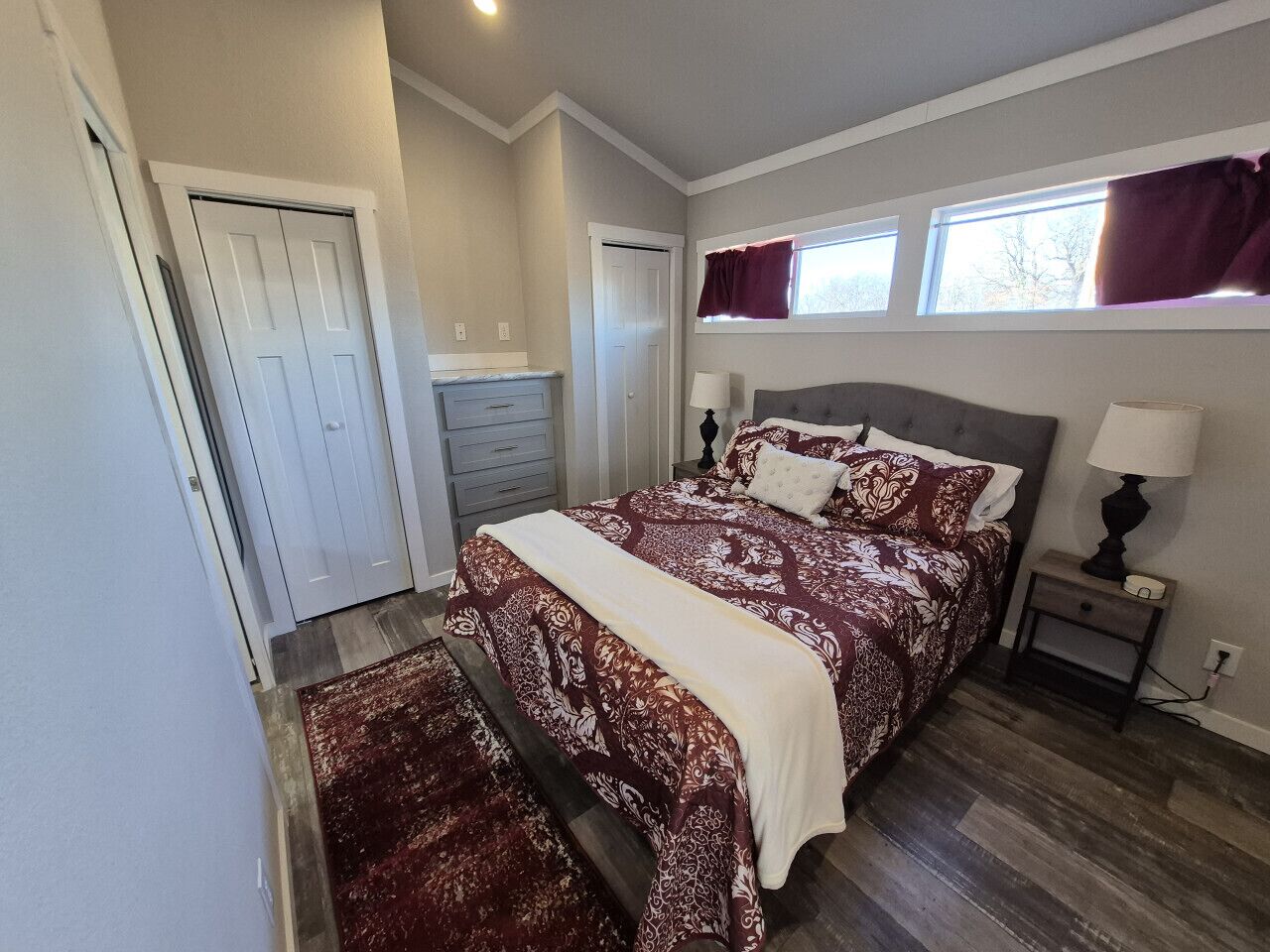 A bedroom with a large bed, a nightstand, a dresser, and a window with curtains.