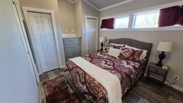 A bedroom with a large bed, a nightstand, a dresser, and a window with curtains.