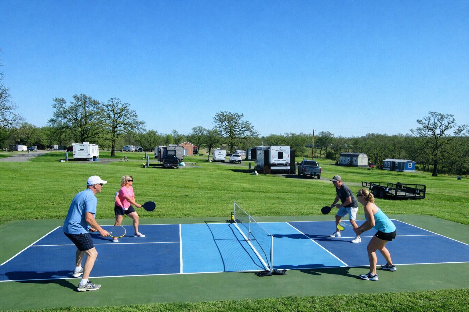 A tennis court with players, surrounded by green grass and trees.