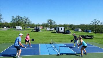 A tennis court with players, surrounded by green grass and trees.