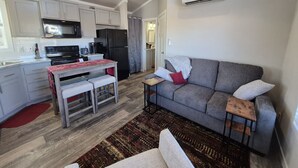Un espacio habitable compacto con kitchenette, un sofá gris, una mesa pequeña y un tapete estampado.