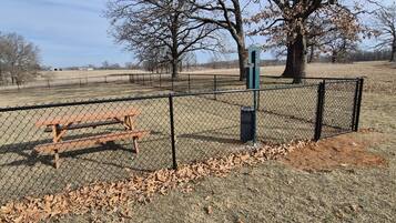 A fenced picnic area with a bench and a trash bin.