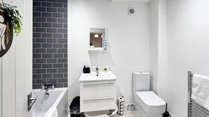 Un bagno moderno con un lavandino bianco, uno specchio, un water e una parete rivestita di piastrelle nere.
