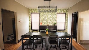 A dining area with a rectangular table, six chairs, a chandelier, and a backdrop of palm leaf wallpaper. - Spacious 5-bedroom house with Wi-Fi and washer/dryer in convenient South Omaha (Omaha)