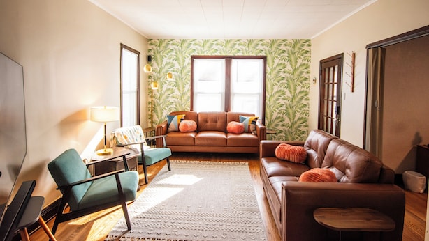 A living room with a brown leather sofa, teal armchair, and a wooden coffee table. There is a patterned wallpaper on the wall and a large window with blinds. - Spacious 5-bedroom house with Wi-Fi and washer/dryer in convenient South Omaha (Omaha)