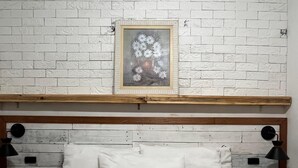 A bedroom with a white brick wall, a wooden headboard, a framed picture, and two bedside lamps. - Colinna Hostel (Rio de Janeiro)