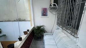 A small, enclosed balcony with a white sofa, a potted plant, and a metal gate. - Colinna Hostel (Rio de Janeiro)