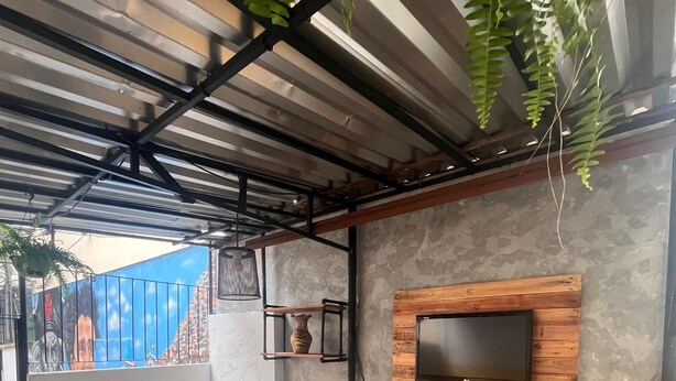 A covered outdoor seating area with a wooden bench, a TV mounted on a wooden panel, and a small table with a vase. - Colinna Hostel (Rio de Janeiro)
