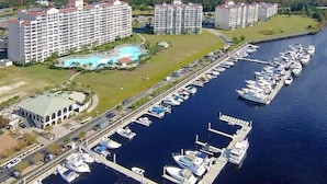 Un port de plaisance où sont amarrés de nombreux bateaux, un grand complexe hôtelier composé de plusieurs bâtiments et un espace piscine.