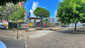 A paved street with cars parked on the side, trees lining the road, and buildings in the background. - Vacanze - Jardim Tropical (Maceió)