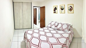 A bedroom with a bed, a door, and three framed floral pictures on the wall. - Vacanze - Jardim Tropical (Maceió)