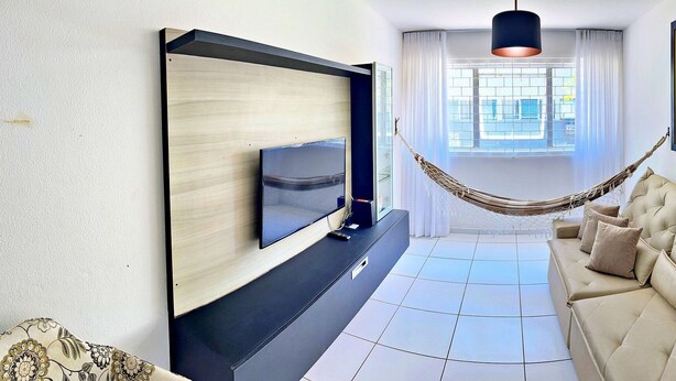 A modern living room with a flat-screen TV, a beige sofa, a hammock, and a colorful abstract painting. - Vacanze - Jardim Tropical (Maceió)