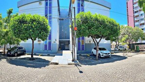 A building with a curved facade, trees in front, and parked cars. - Vacanze - Jardim Tropical (Maceió)