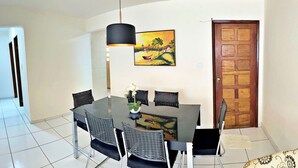 A dining area with a round table, black chairs, a hanging light, and a painting on the wall. - Vacanze - Jardim Tropical (Maceió)