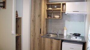 A compact kitchen with wooden cabinets, a built-in sink, a stove, and a small countertop. - Camping Charlieu - Nos Studios (Charlieu)
