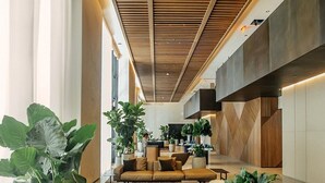 En moderne lobby med et træribbet loft, et centralt siddeområde med sofaer og et sofabord, samt store potteplanter.