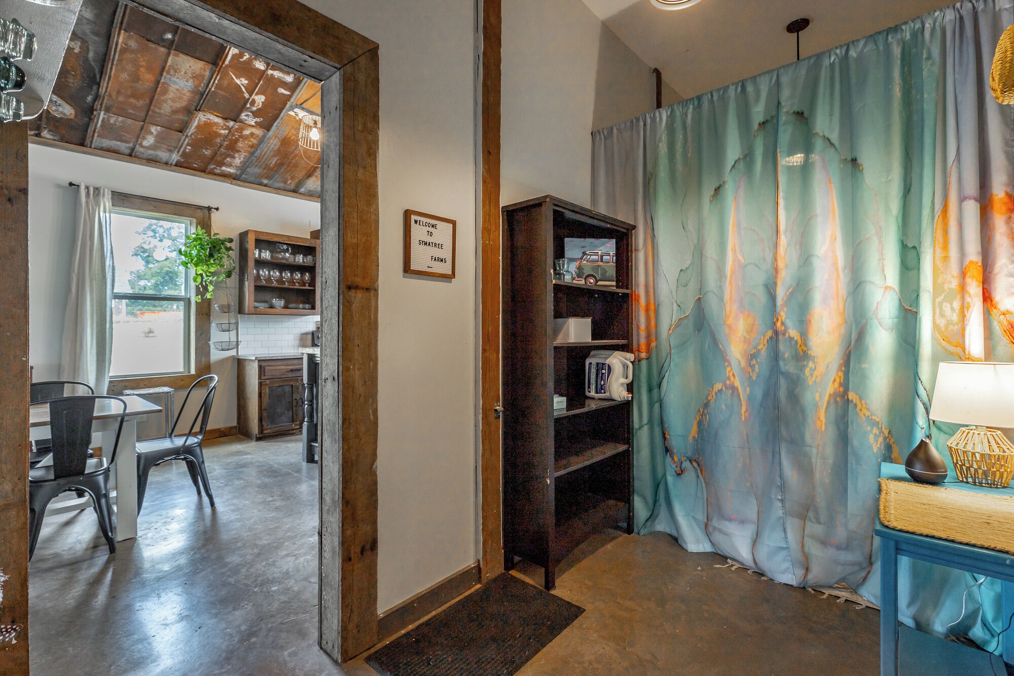 Une pièce avec une porte en bois donnant sur une cuisine, une bibliothèque et un rideau bleu à motifs marbrés.