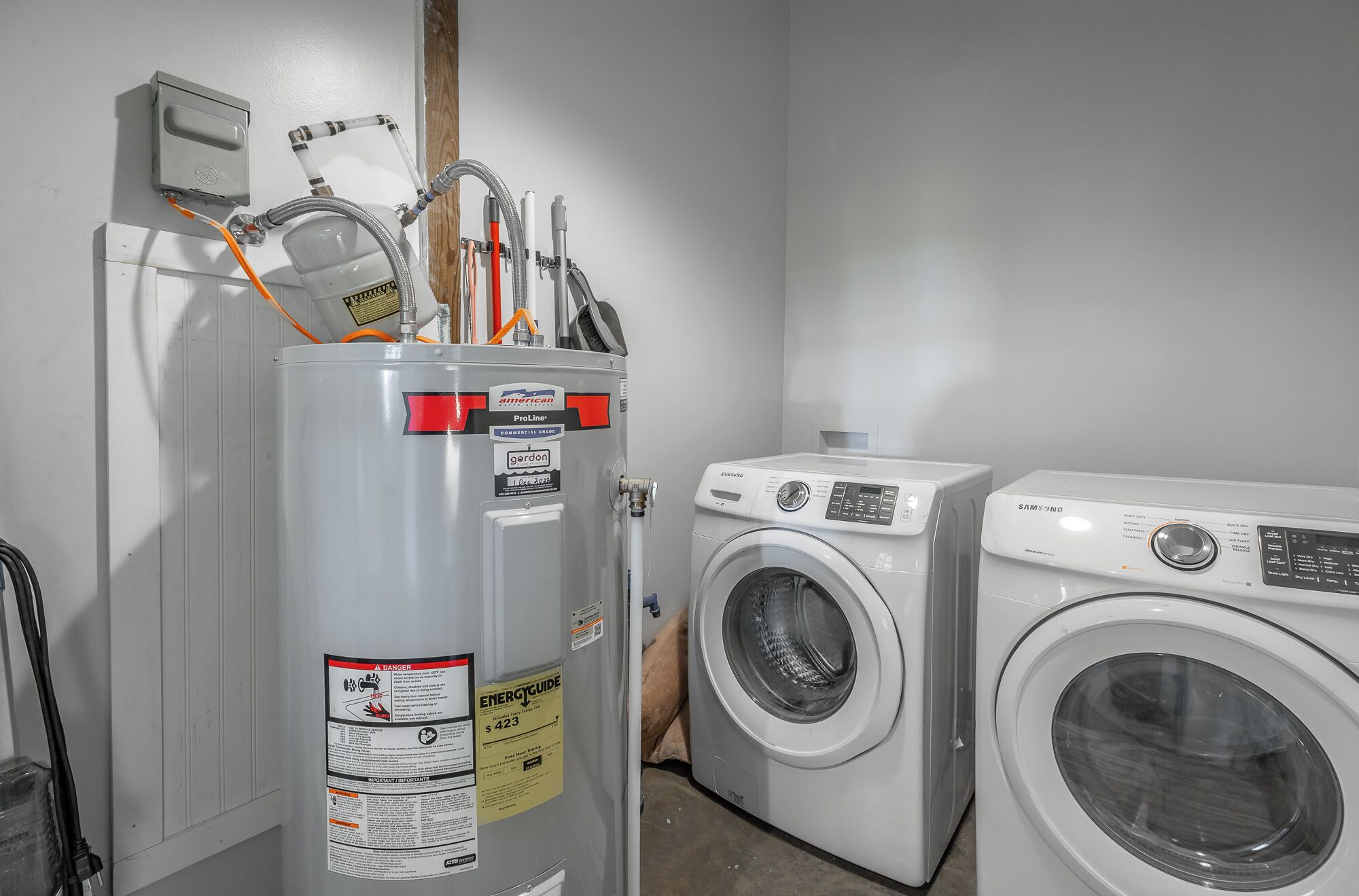 A laundry area with a water heater, washing machines, and a utility meter.