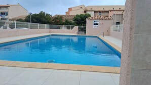 A rectangular swimming pool with a tiled deck, surrounded by a white fence.