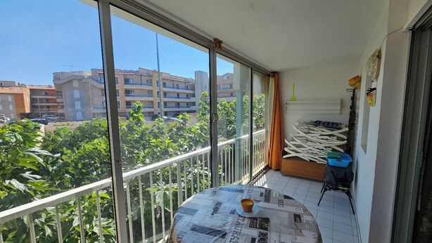A balcony with a table, chairs, and a view of buildings and greenery.