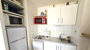 A compact kitchen with a refrigerator, microwave, stove, sink, and white cabinets.
