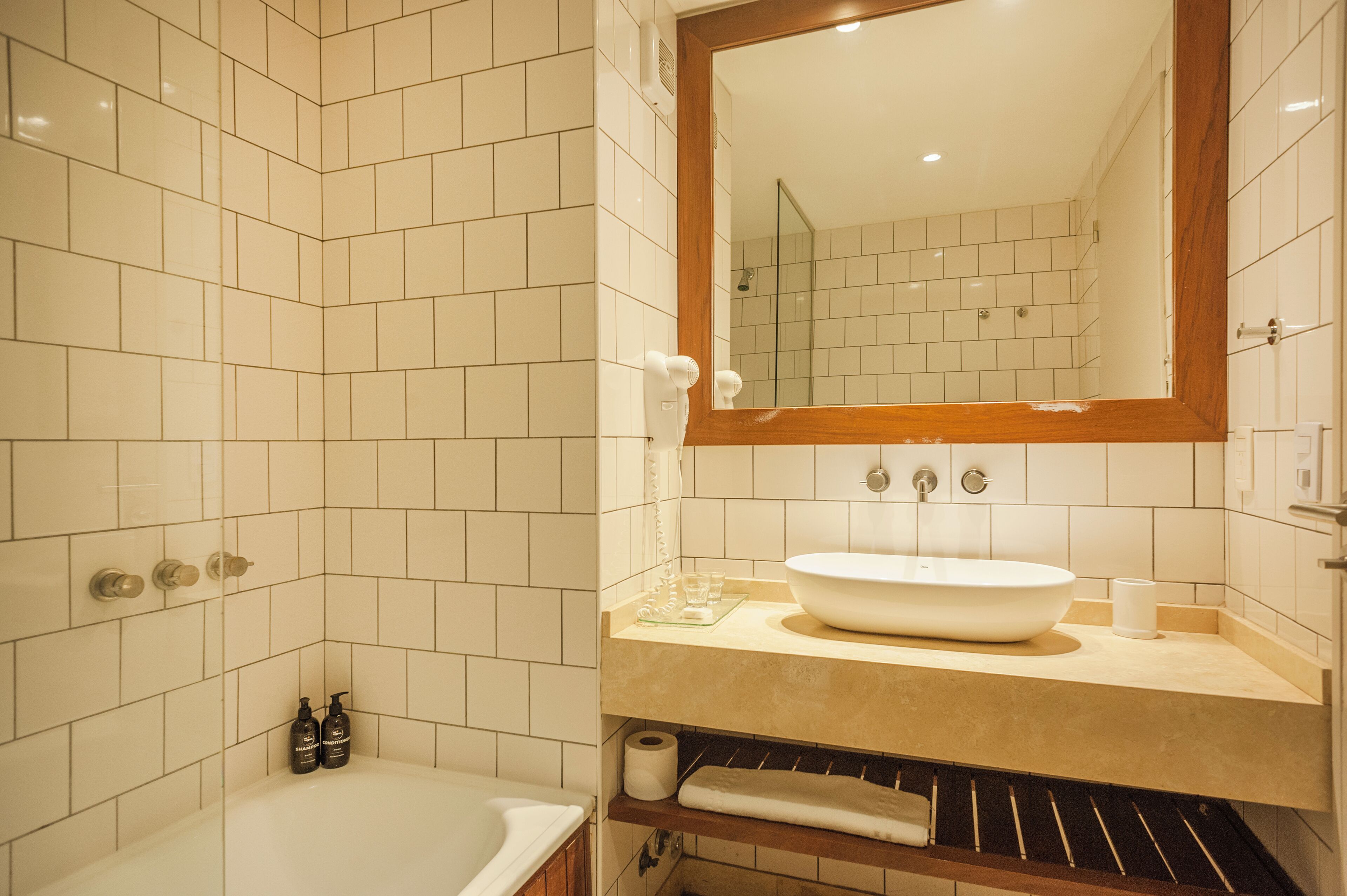 A bathroom with white tiles, a large mirror, a sink, and a bathtub.