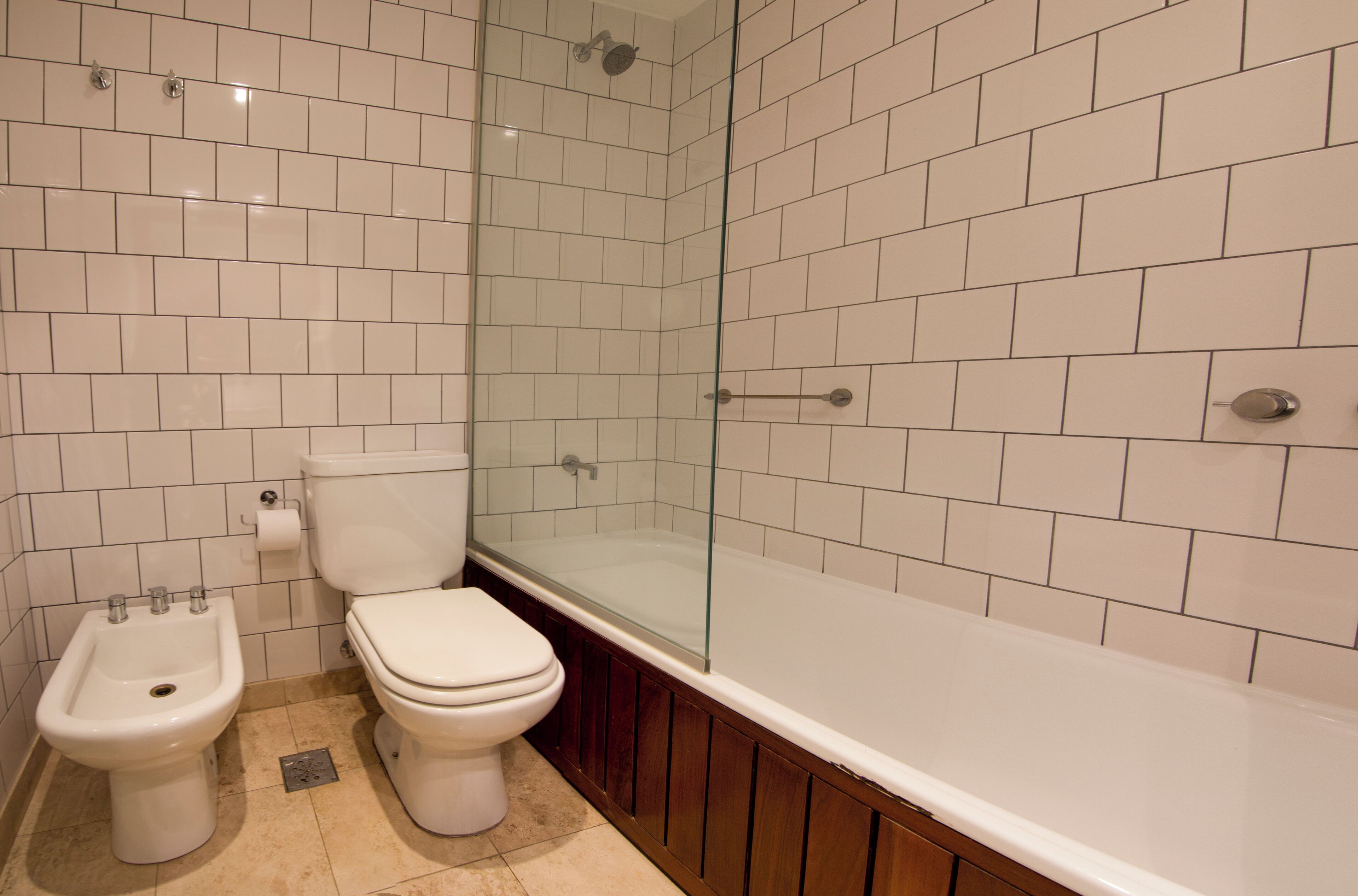 A bathroom with white tiled walls, a glass-enclosed shower, a white toilet, and a bidet.