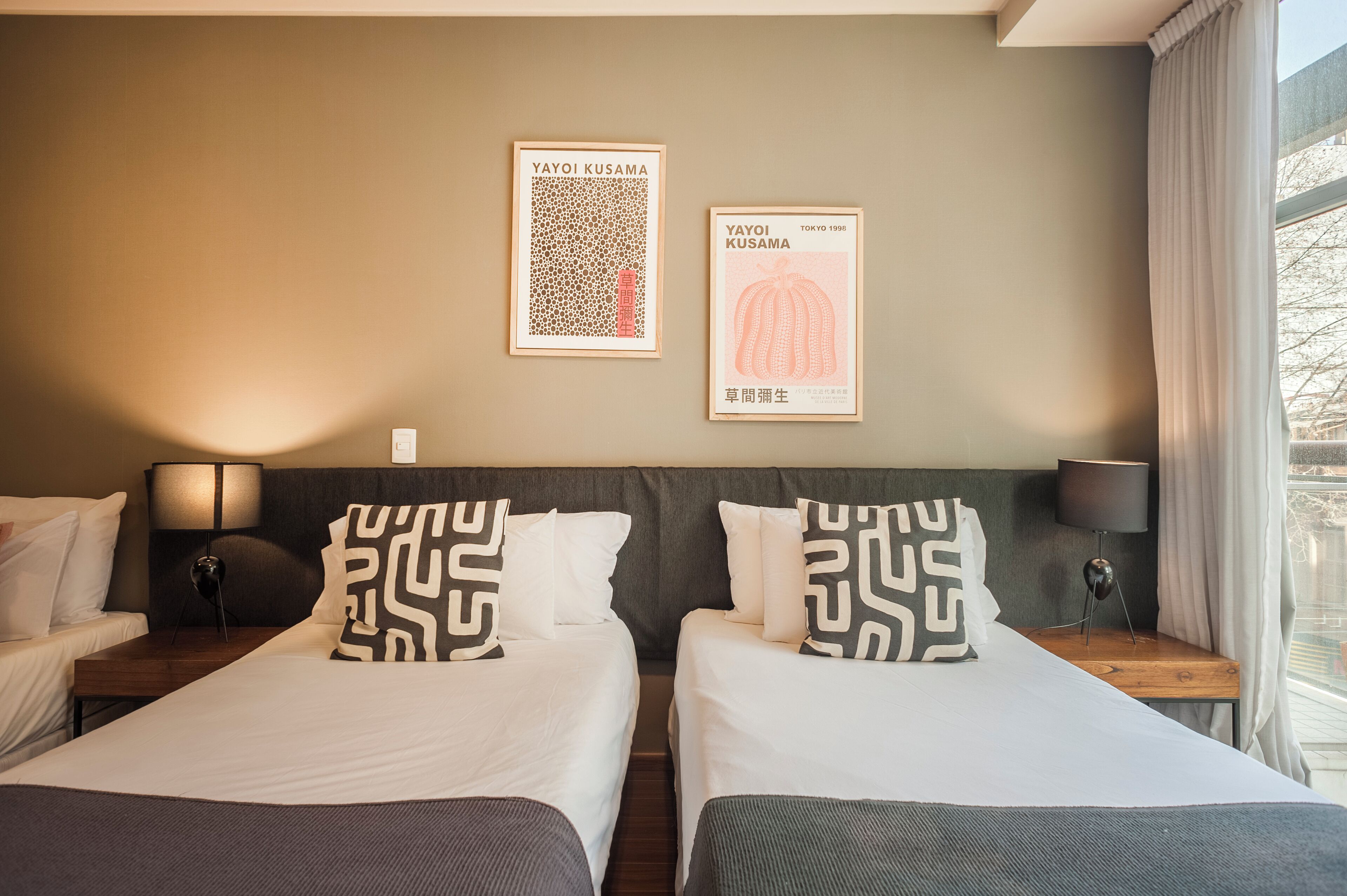 Ein Hotelzimmer mit zwei Betten, einem Nachttisch mit Lampe und zwei gerahmten Postern an der Wand.