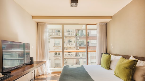 A hotel room with a large bed, a TV on a wooden console, and a balcony with a view of other buildings. - Modern Premium Studio T310 (Buenos Aires)