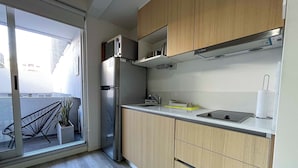 A modern kitchen with wooden cabinets, a stainless steel refrigerator, and a sliding glass door leading to a balcony with a chair and plant. - Maison Thames by Argenhost (Buenos Aires)