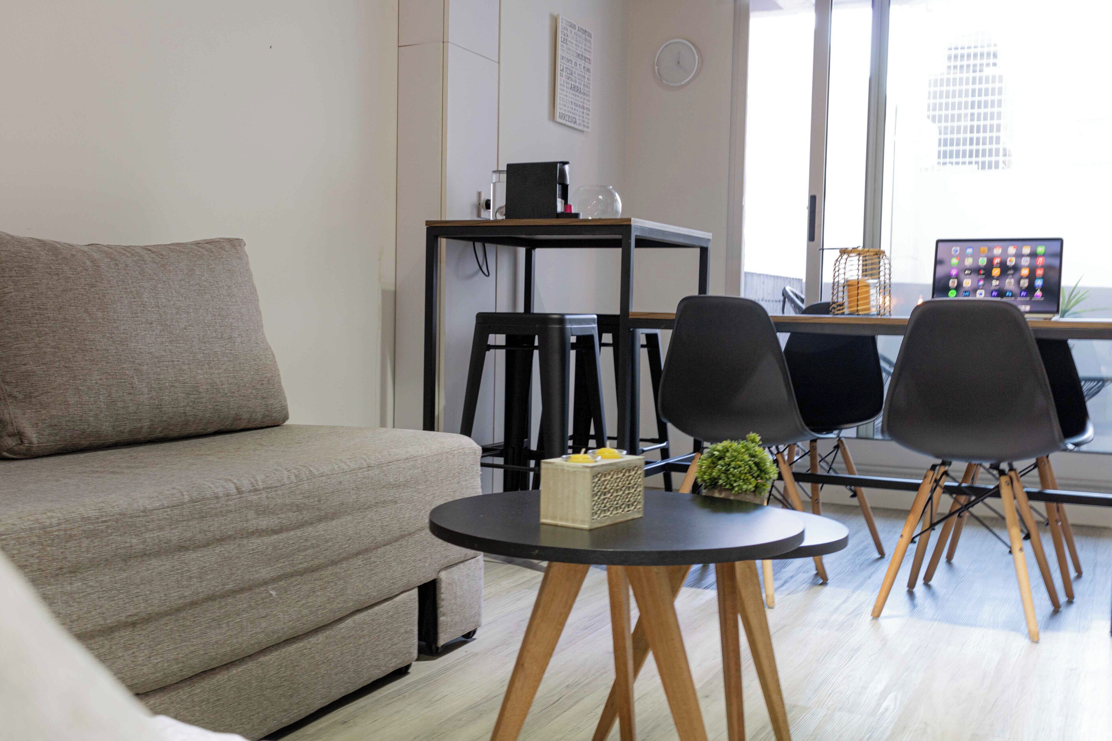 A modern living room with a sofa, a round table, and a desk with a laptop.
