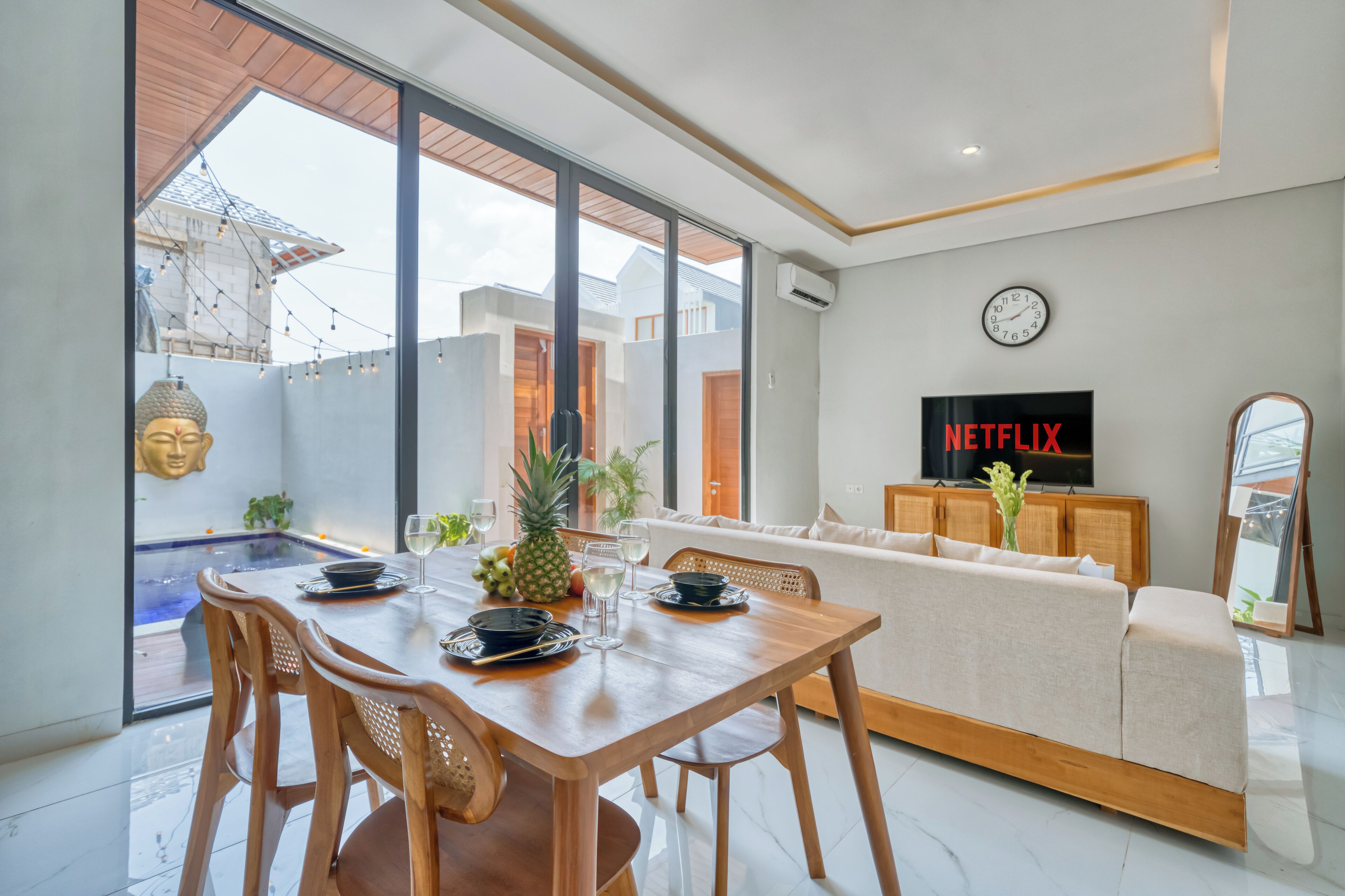 A modern living room with a wooden dining table, a sofa, and a TV displaying 'NETFLIX'.
