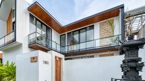 A modern two-story building with a white facade, large windows, and a wooden balcony. - Cozy 3bedroom villa Bliss, Close to Canggu,
King bed,Tranquil! (Bali)