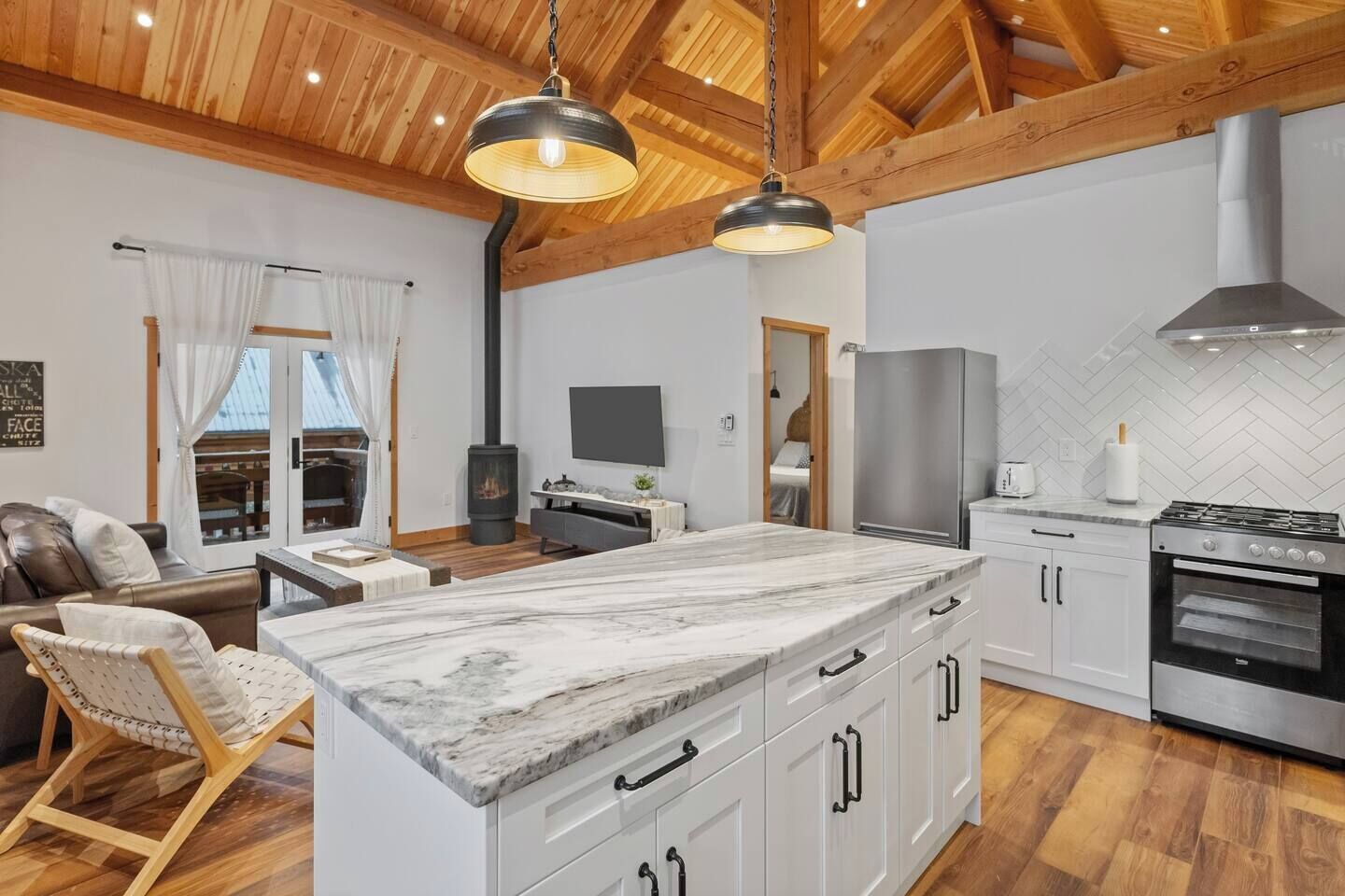 A modern kitchen with a marble island, wooden ceiling beams, and a built-in stove.