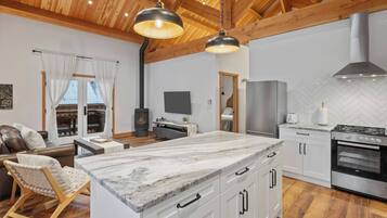 A modern kitchen with a marble island, wooden ceiling beams, and a built-in stove.
