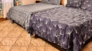 Een slaapkamer met een houten plafond, een bed met beddengoed met een patroon, en gordijnen met een tropisch bladmotief.