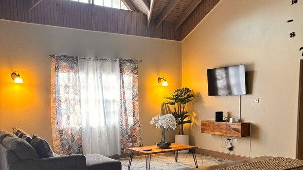 Een ruime woonkamer met een bank, een salontafel en een aan de muur bevestigde televisie.