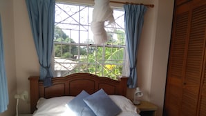 Un dormitorio con una cama de madera, dos almohadas, una lámpara de noche y una ventana con cortinas.