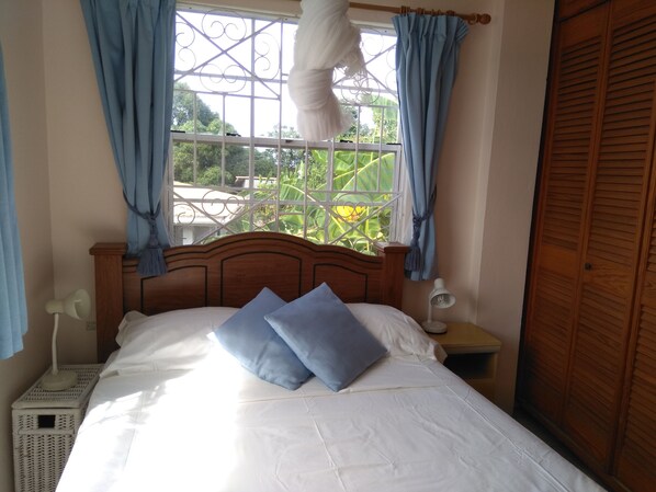 A bedroom with a wooden bed, two pillows, a bedside lamp, and a window with curtains.
