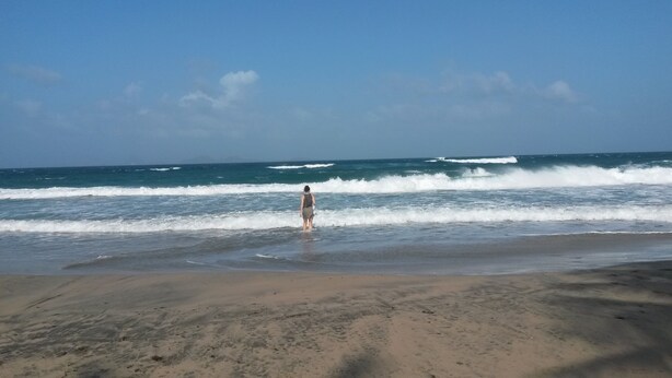 Una playa con una persona de pie en el agua, olas rompiendo sobre la orilla.