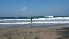 A beach with a person standing in the water, waves crashing onto the shore.