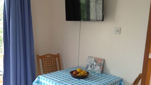Un comedor con mantel a cuadros, un cuenco de fruta y un televisor montado en la pared.
