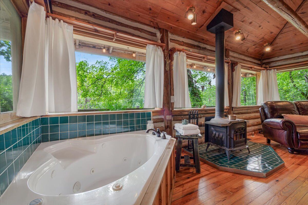 L’intérieur d’une cabane en rondins, avec une grande baignoire, un poêle à bois et un canapé en cuir.