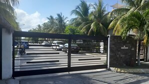 A gated entrance with a metal gate, a paved driveway, and palm trees in the background. - Beach house with jacuzzi (Playa del Carmen)