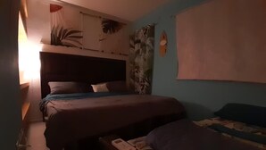 A room with two beds, a wall with a tropical mural, and a small table with a device. - Beach house with jacuzzi (Playa del Carmen)