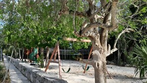 A tree-lined pathway with swings and a stone wall. - Beach house with jacuzzi (Playa del Carmen)