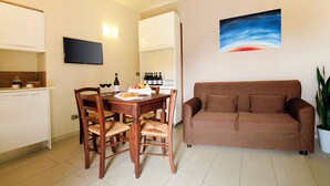 A modern living room with a brown sofa, wooden dining table, and chairs. A flat-screen TV is mounted on the wall, and a painting is displayed above the sofa. - Apartment with balcony - La Rosa nel Borgo (La Morra)